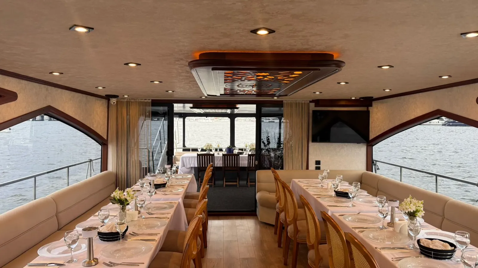 Dinner tables set in the glass salon of a yacht with the Bosphorus visible through the windows