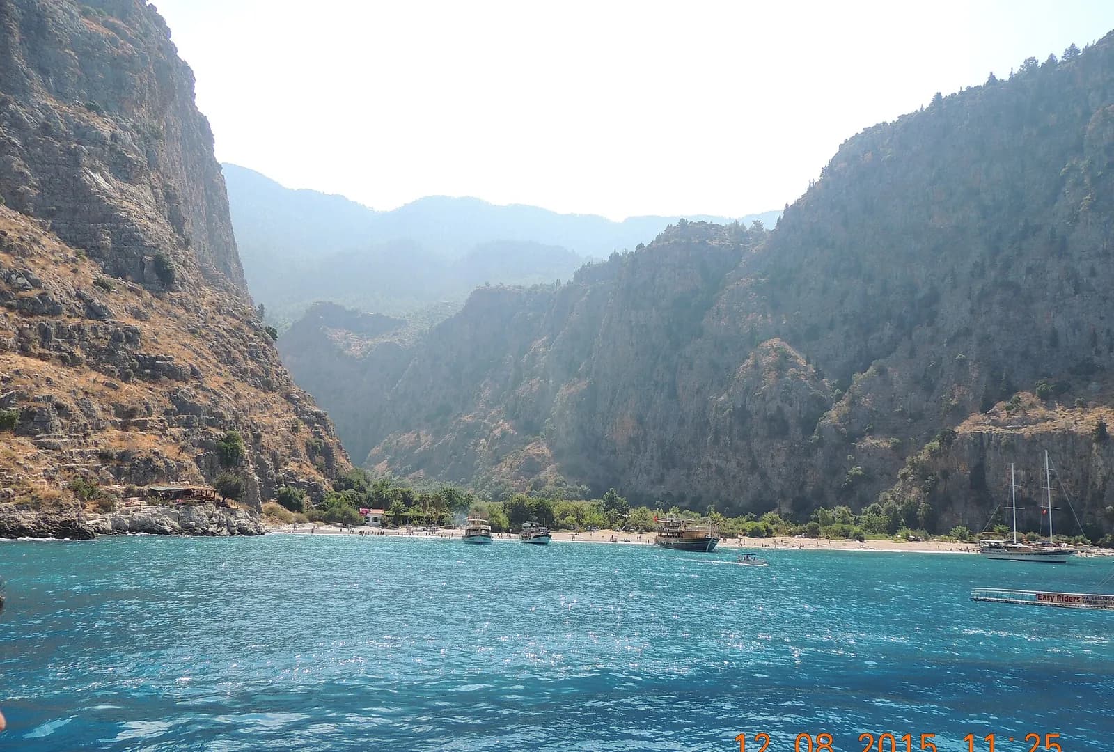 Approaching Butterfly Valley from the sea: the cove, beach and anchored boats at the foot of the cliffs