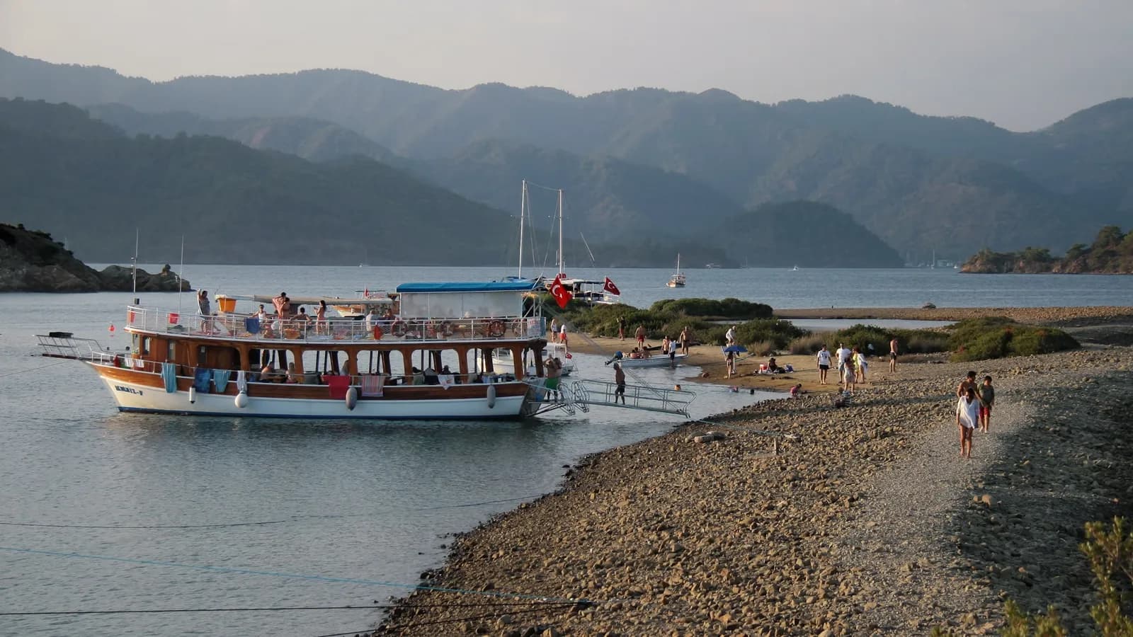 A boat anchored at the Yassica Islands, pebble beach and gulf in evening light
